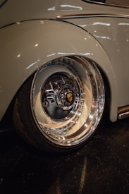 A close-up view of a shiny, polished car wheel with a prominent logo at the center. The surrounding car body is smooth, reflecting light in a garage or showroom setting.