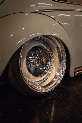 A close-up view of a shiny, polished car wheel with a prominent logo at the center. The surrounding car body is smooth, reflecting light in a garage or showroom setting.