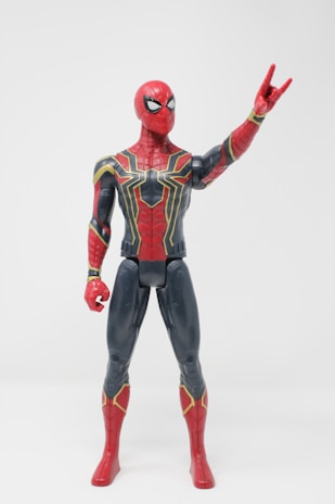 A detailed action figure of a superhero in a red and dark blue armored suit, featuring intricate gold lines across the chest. The figure is posed with one hand raised and some fingers extended, expressing a dynamic stance.