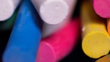 Colored chalk sticks are arranged closely together, showcasing a variety of vibrant colors including blue, pink, yellow, and white. The chalk is cylindrical and appears slightly worn, indicative of prior use.