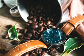A stylish wristwatch with a leather strap resting on a wooden table beside a cup of coffee.