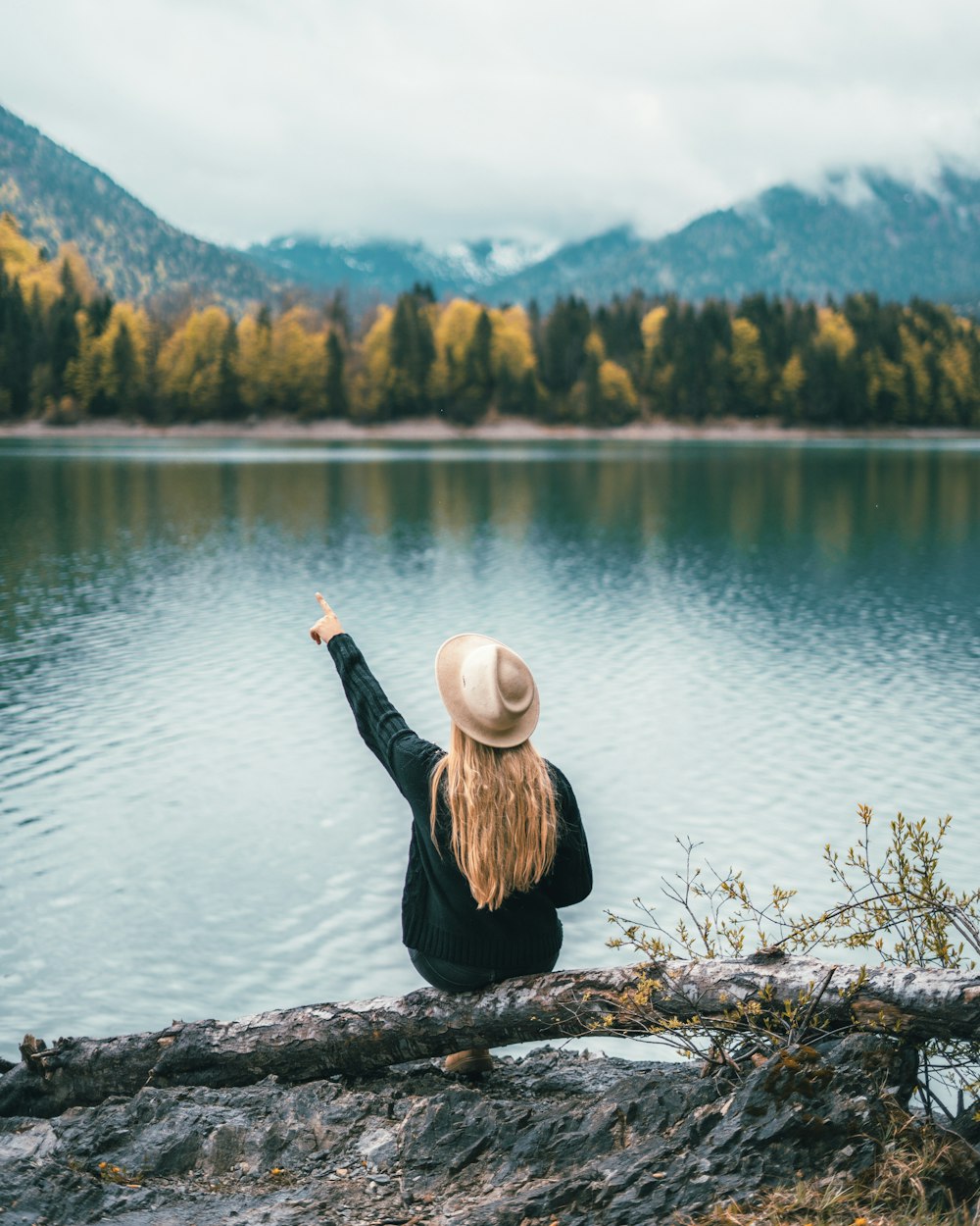 woman in green hoodie sitting on tree bark near lake