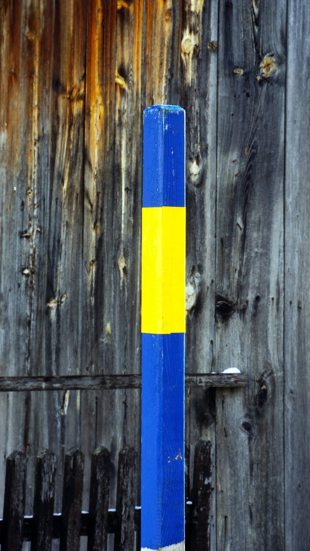 a blue and yellow pole next to a wooden fence