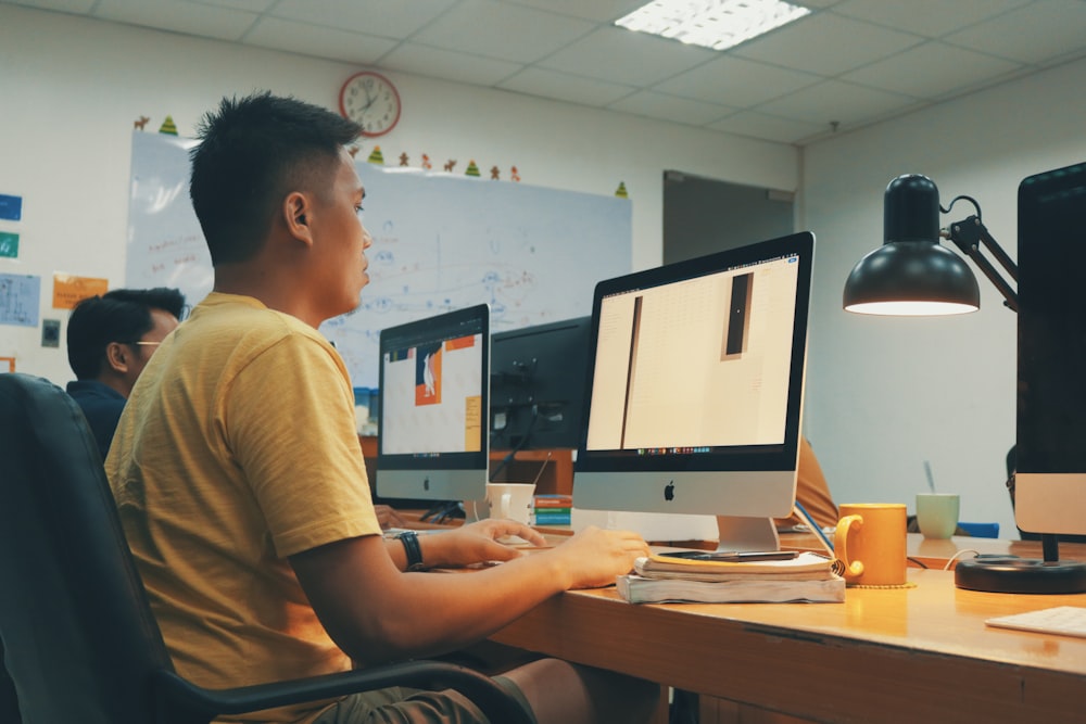 man using Apple desktop inside room beside man