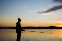 An angler casting a line into a serene lake at sunrise, embodying the spirit of adventure and connection with nature.