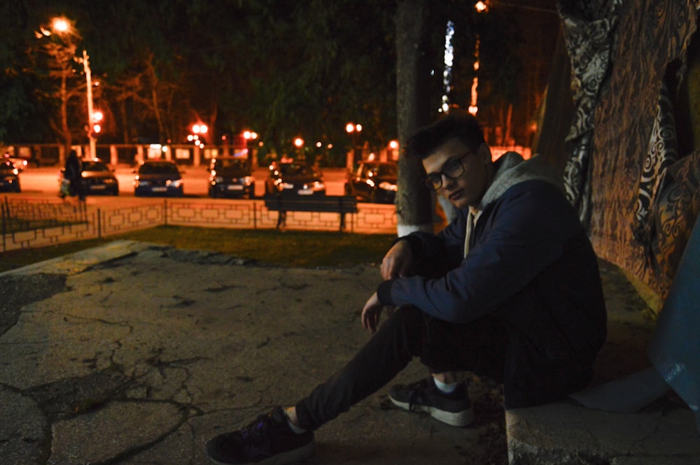 man sitting on grey surface wearing jacket during nighttime