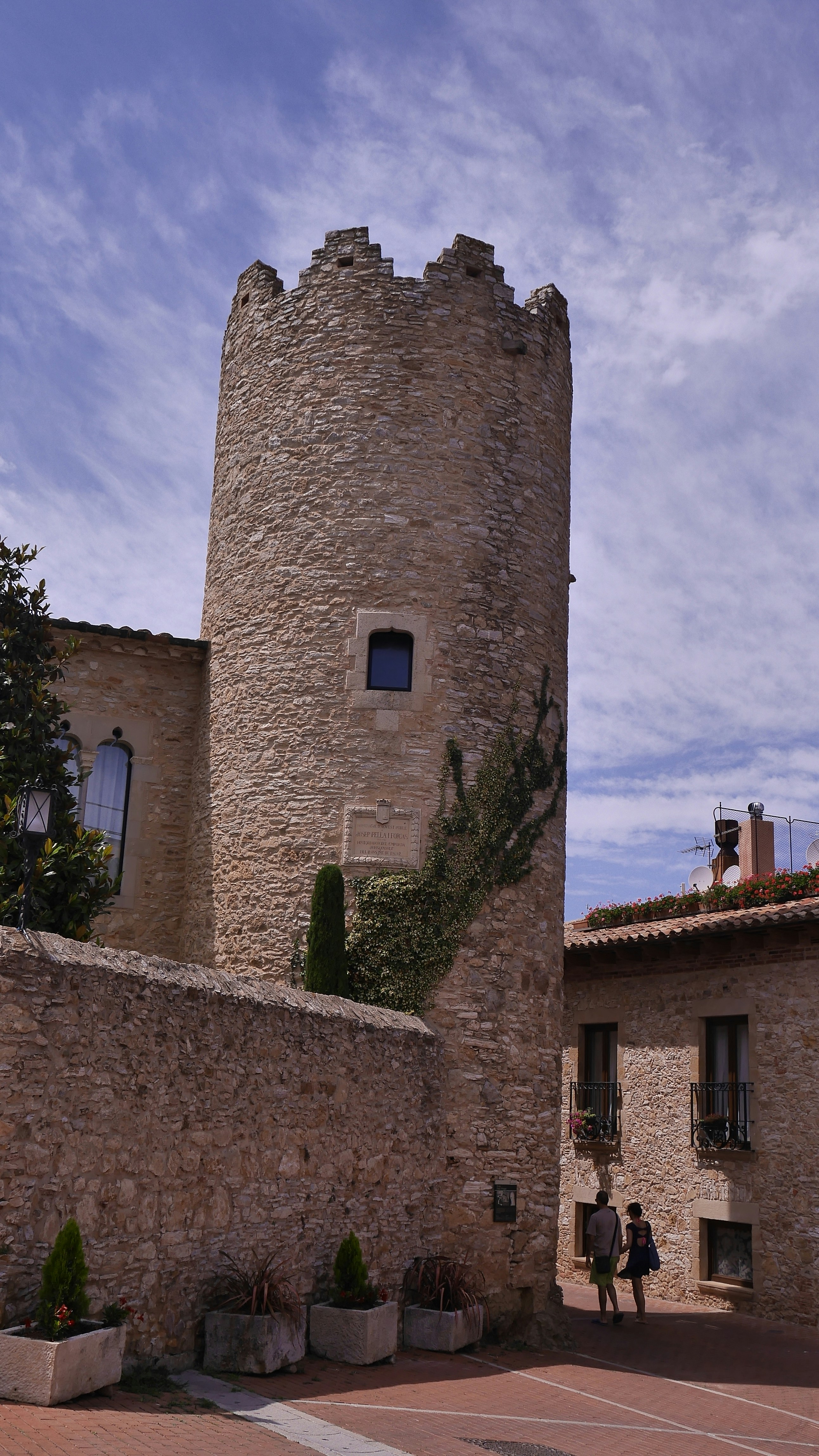 two persons walking beside gray brick tower and building