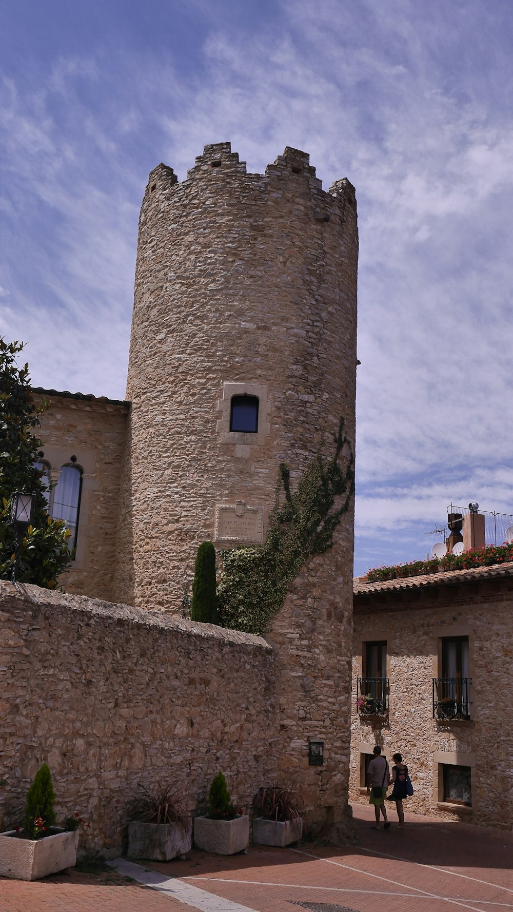 two persons walking beside gray brick tower and building