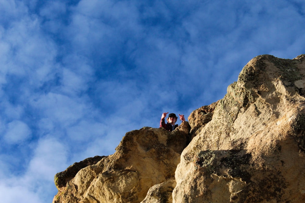 person on rock mountain under blue and white sky