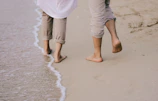 Couple walking barefoot along a sandy shore with colorful sun umbrellas.