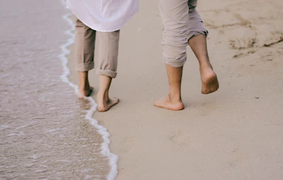 Couple walking barefoot along a sandy shore with colorful sun umbrellas.