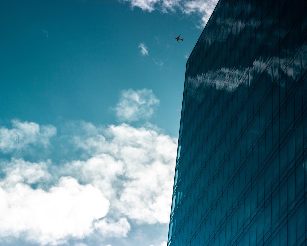 blue glass walled building showing airplane under white and blue skies