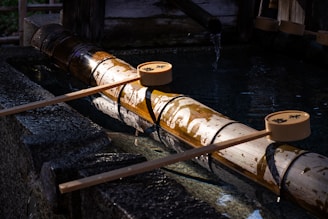 A traditional Japanese water basin made of bamboo and stone, with ladles resting on top. Water trickles from a bamboo spout into the basin, creating a serene and calming atmosphere.