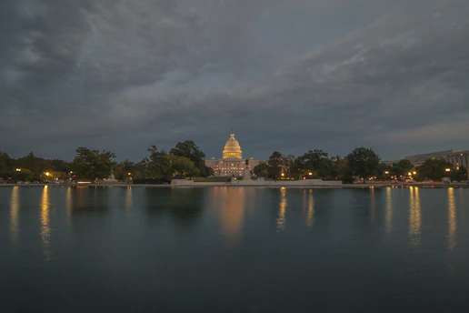 A dignified view of the Virginia State Capitol bathed in soft morning light, framed by historic oak trees.