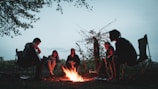 A peaceful campsite with a campfire surrounded by chairs at dusk.