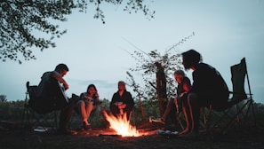 A peaceful campsite with a campfire surrounded by chairs at dusk.