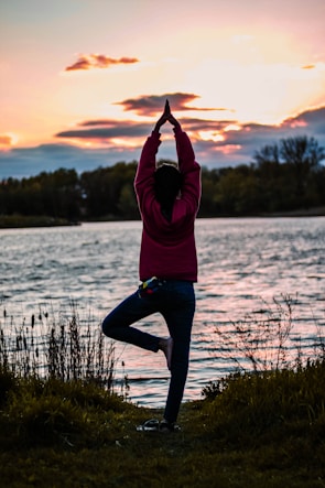 A person practicing yoga outdoors during sunrise, surrounded by nature.