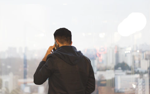 A close-up of a business professional using a VoIP phone with a cityscape in the background.