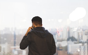 Agent on a phone call, standing by a window with city views behind.