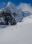 Snow-covered alpine peak with skiers descending under a clear blue sky.