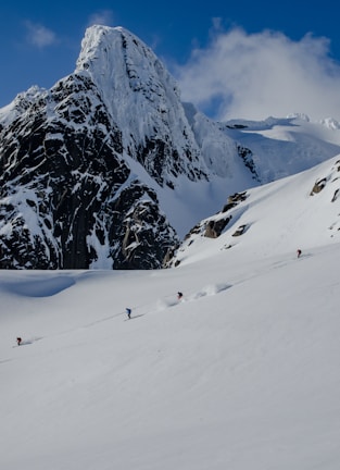 Snow-covered alpine peak with skiers descending under a clear blue sky.