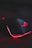 A sleek gaming mouse with a black finish and red backlighting. The mouse features a glowing logo on the top and an illuminated edge, placed on a surface with a subtle circuit-like pattern.