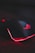 A sleek gaming mouse with a black finish and red backlighting. The mouse features a glowing logo on the top and an illuminated edge, placed on a surface with a subtle circuit-like pattern.