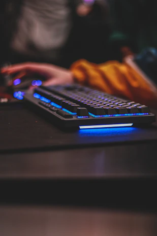 Close-up of a gamer’s hands on a futuristic neon-lit keyboard and mouse.