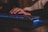 Close-up of hands typing on a keyboard with neon blue lighting in the background.