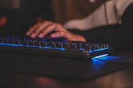 Close-up of hands typing on a keyboard with soft purple-blue lighting in the background.
