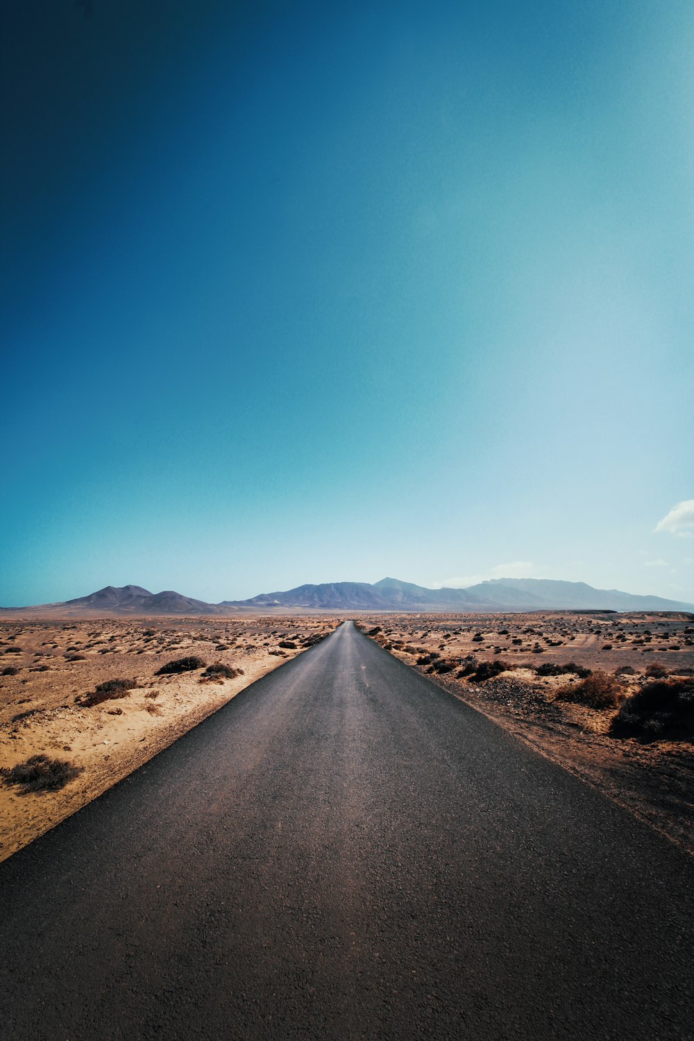 Route goudronnée grise sans véhicule près d’un champ brun sous un ciel bleu et blanc