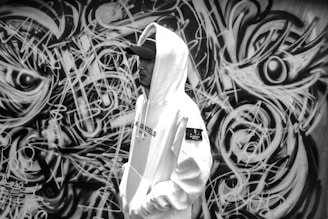 A stylish streetwear outfit featuring a hoodie and cap, set against a graffiti wall.