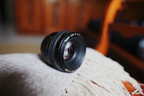 A high-quality camera lens resting on a textured fabric background.