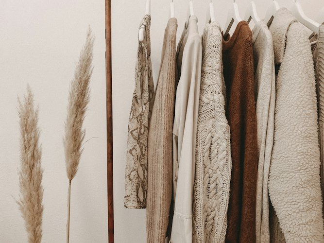 Stylist arranging clothing items and accessories on a rack while reviewing a laptop