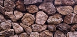 A wall composed of irregularly shaped stones, fitted together closely without mortar. The stones are various shades of brown and gray, exhibiting a rough, textured surface.
