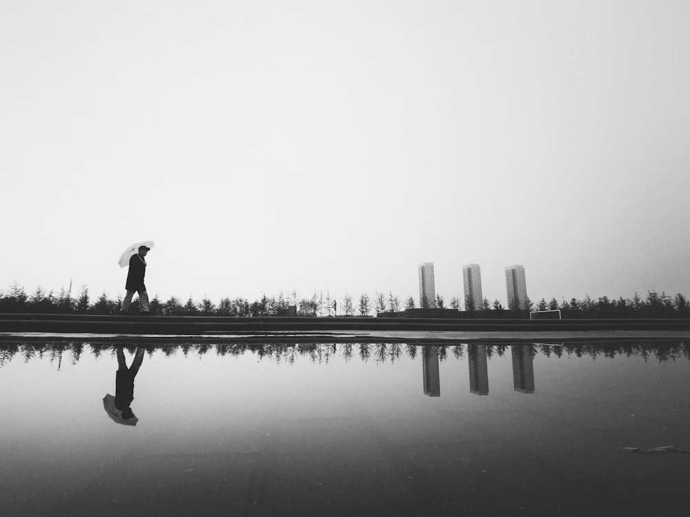 silhouette photography of man holding umbrella beside body of water