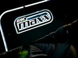 A row of empty black theater seats is shown beside a large illuminated sign displaying 'GSC maxx' against a dark background.