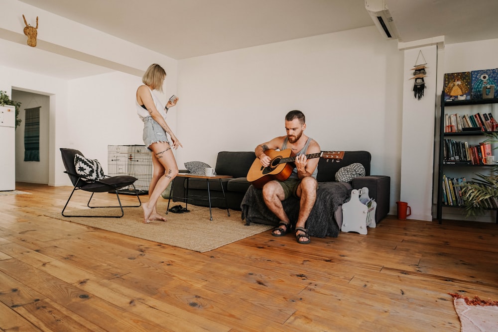 man playing guitar sitting on sectional sofa near standing woman