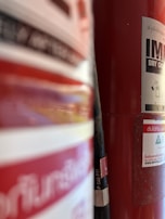 A close-up view of a red fire extinguisher with partially visible labels, hose, and some text in a foreign language. The background is slightly out of focus, emphasizing the fire extinguisher's details.