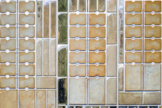 An aerial view of a series of rectangular plots, likely salt flats or evaporation pools, arranged in a grid pattern. Each section varies in color and texture, possibly indicating different stages of evaporation or mineral concentration.