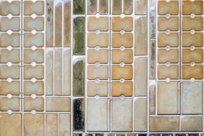 An aerial view of a series of rectangular plots, likely salt flats or evaporation pools, arranged in a grid pattern. Each section varies in color and texture, possibly indicating different stages of evaporation or mineral concentration.