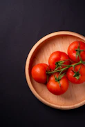 five tomatoes in round brown wooden platet