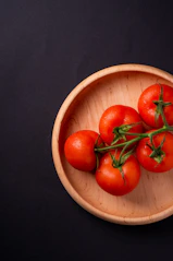 five tomatoes in round brown wooden platet