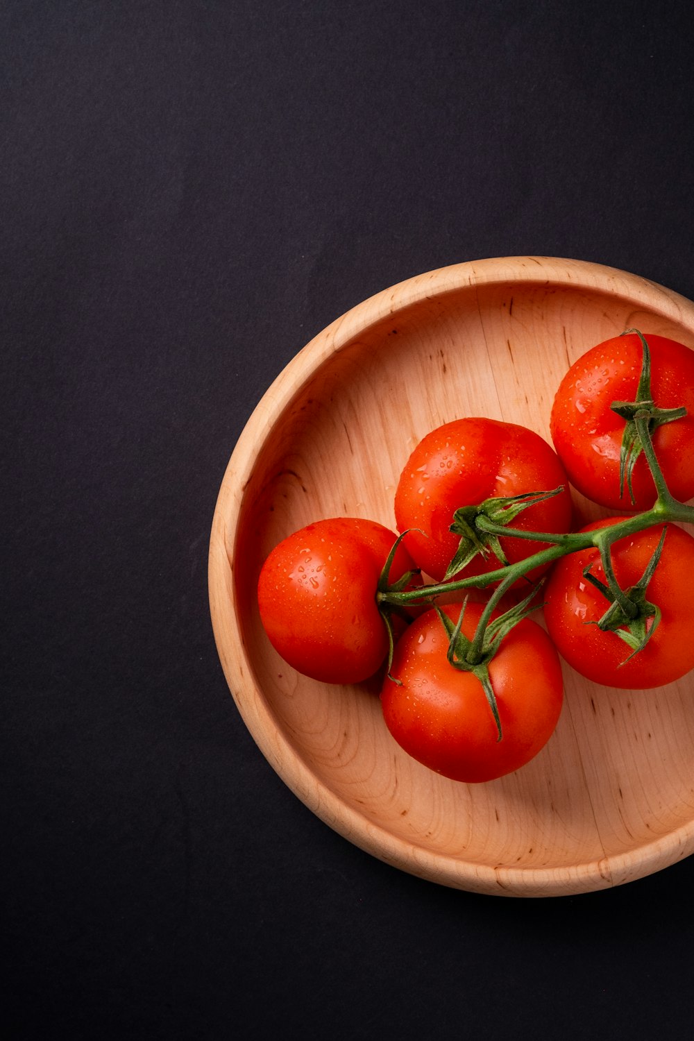 five tomatoes in round brown wooden platet