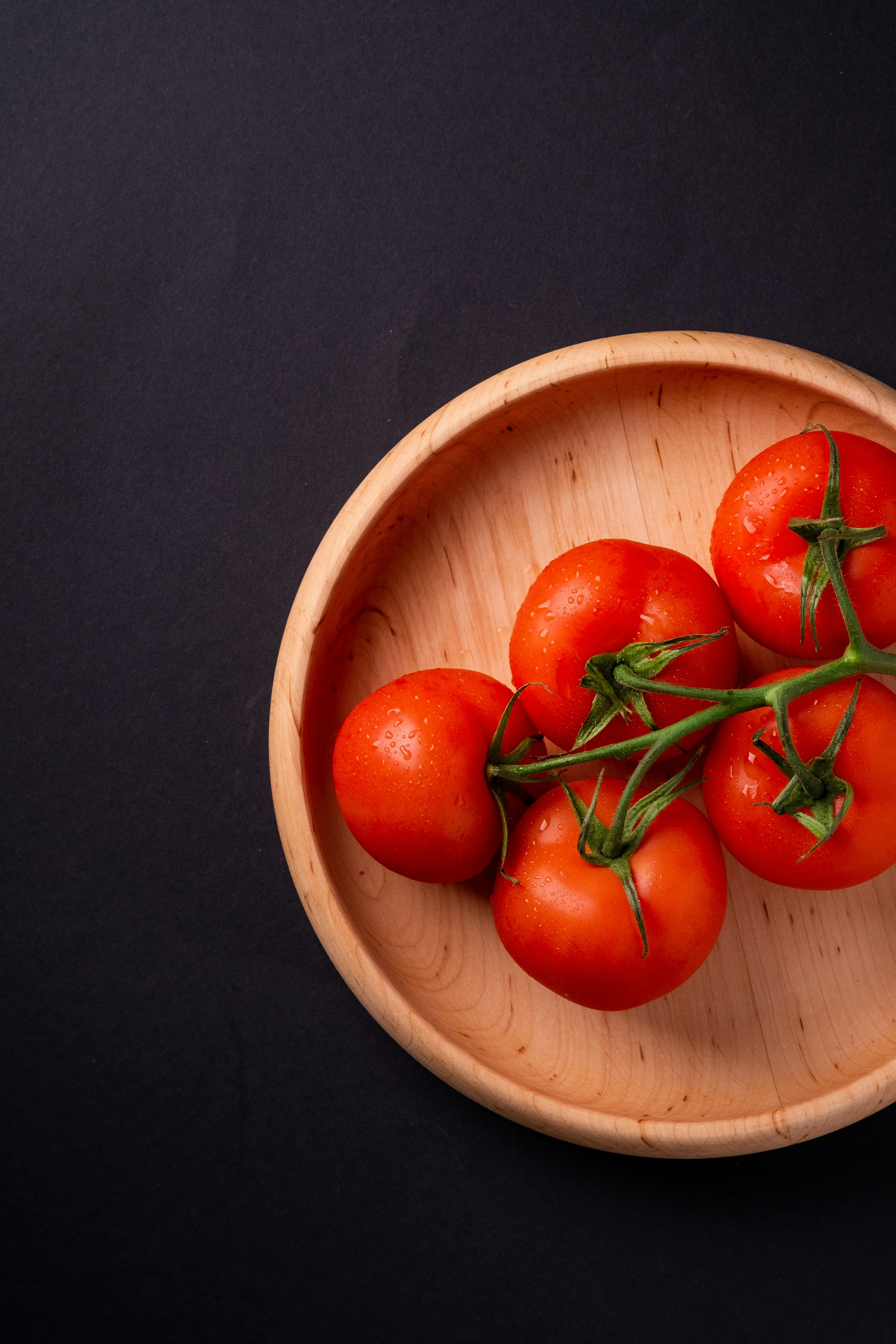five tomatoes in round brown wooden plate
