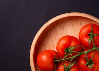 five tomatoes in round brown wooden platet