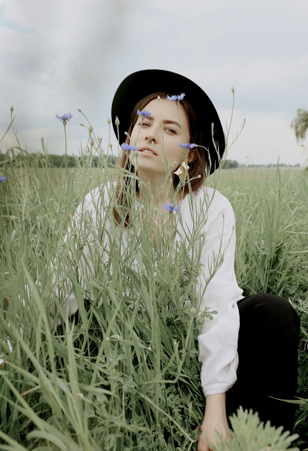 Frau mit schwarzem Hut und weißem langärmeligem Oberteil in der Nähe von Pflanzen
