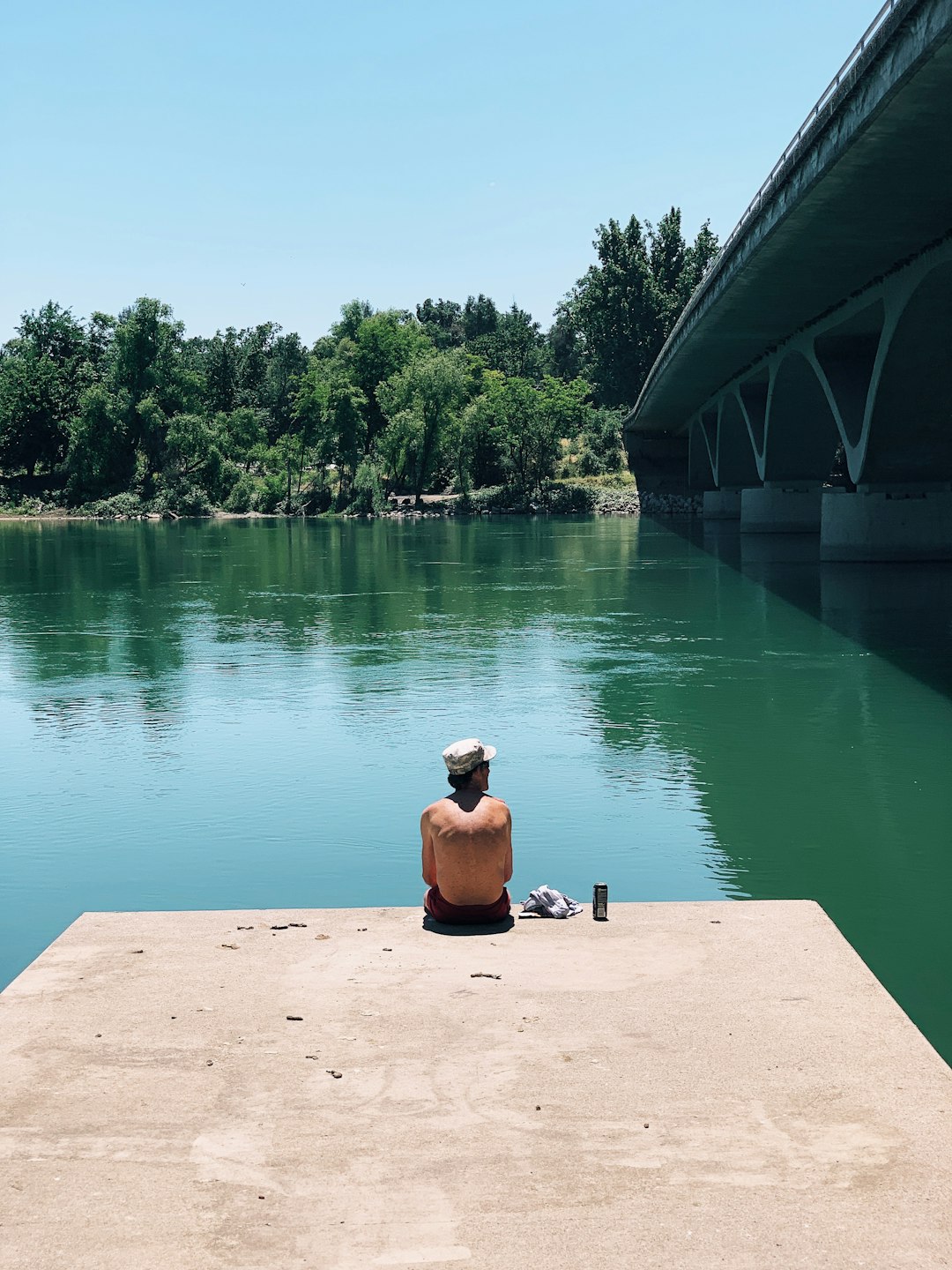 man sitting on concrete dock beside river