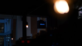 A dimly lit indoor environment with an illuminated 'GRAPH' sign in the background. Warm overhead lights create a cozy atmosphere, with a focus on the contrast between darkness and the bright sign.