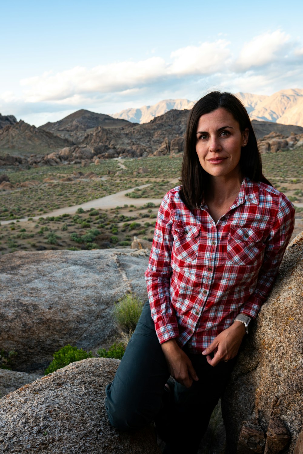 woman standing near rock formation in green open field under white and blue skies